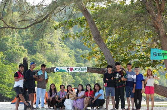 Un groupe de jeunes assis et debout devant un arbre sur la plage