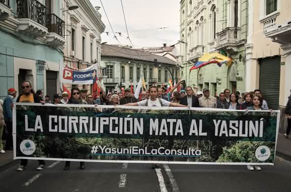 Un cortège défile dans une rue avec une grande banderole portant le slogan, en espagnol, « La corruption tue le Yasuní »