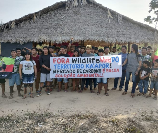 30 indigènes manifestent devant une hutte : « Wildlife Works, sortez du territoire des Ka’apor. Le commerce du carbone n’est pas une solution environnementale viable »