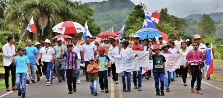 Manifestation contre l’exploitation minière dans la province de Veraguas au Panama Des personnes défilent sur une route de campagne au Panama avec des bannières, des drapeaux du Panama et des parapluies assortis