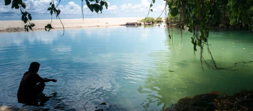 L’île de Célèbes (Sulawesi) compte 6 000 kilomètres de côtes ponctuées de plages de sable, d’escarpements rocheux et de baies tranquilles Une femme est assise dans l’eau dans une baie bordée de sable et de rochers
