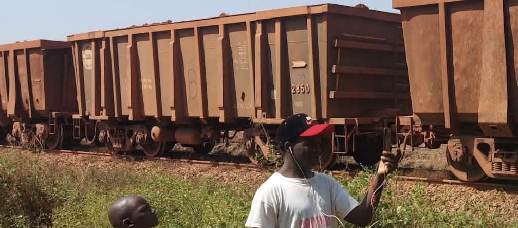 Bauxite guinéenne en route vers le port Train de marchandises, avec un jeune garçon et un homme au premier plan