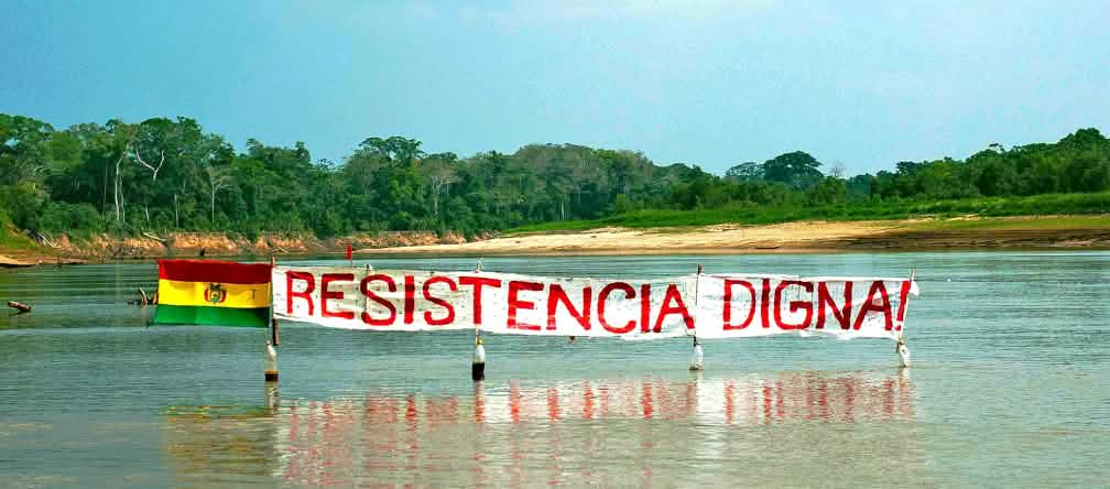 Les habitants du parc national de TIPNIS protestent contre le projet de construction de route dans la forêt tropicale Bannière sur un fleuve dans la forêt tropicale de Bolivie : « Résister est une question de dignité » peut-on lire sur la bannière à côté du drapeau bolivien