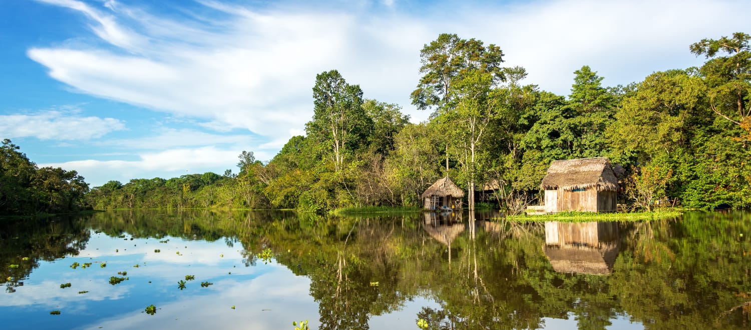 La forêt amazonienne et une cabane en bois se reflètent dans l’eau du fleuve Yanayacu au Pérou