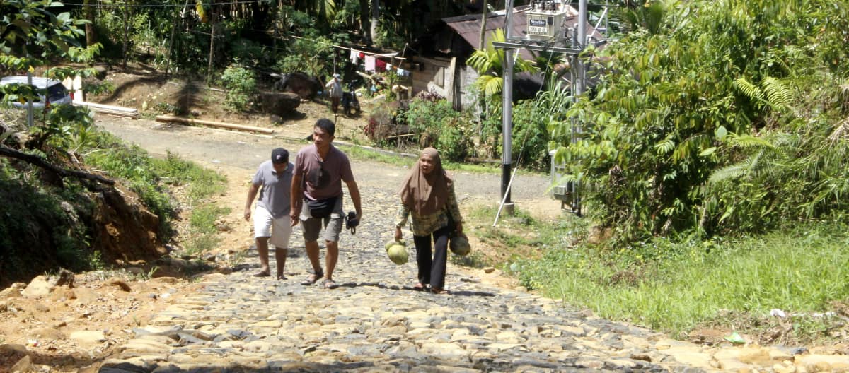 Trois personnes sur une route pavée dans un village en forêt