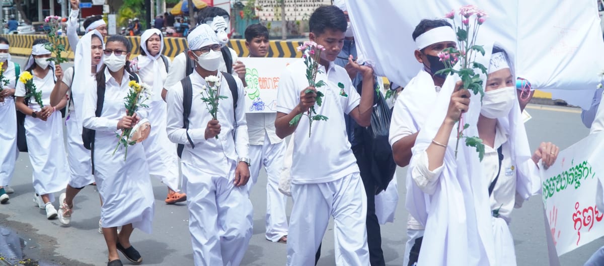 Des jeunes gens vêtus de blanc et tenant des fleurs à la main défilent dans une rue de Phnom Penh