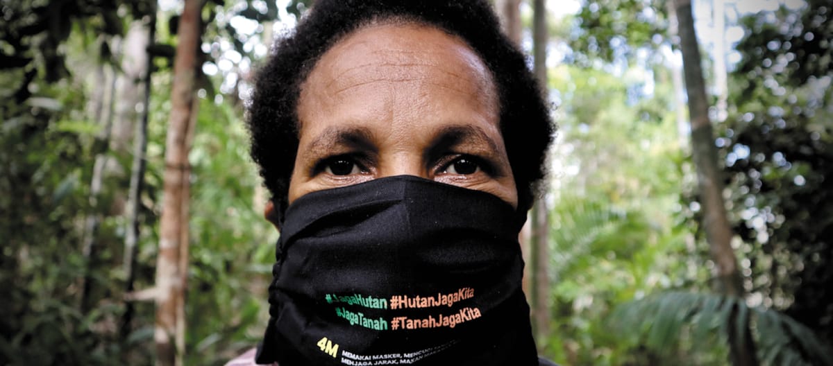 Papoue portant un masque noir sur lequel est écrit : « Protégeons la forêt. La forêt nous protège. »