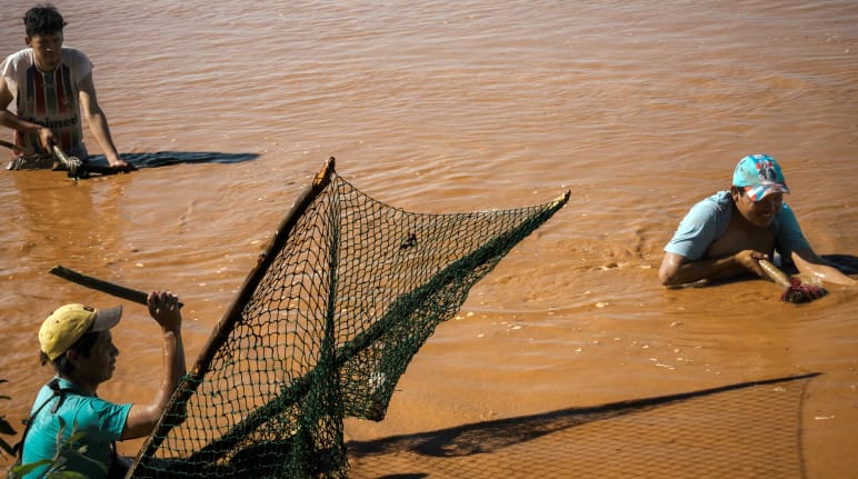 Trois hommes pêchent dans les eaux brunes d’un lac